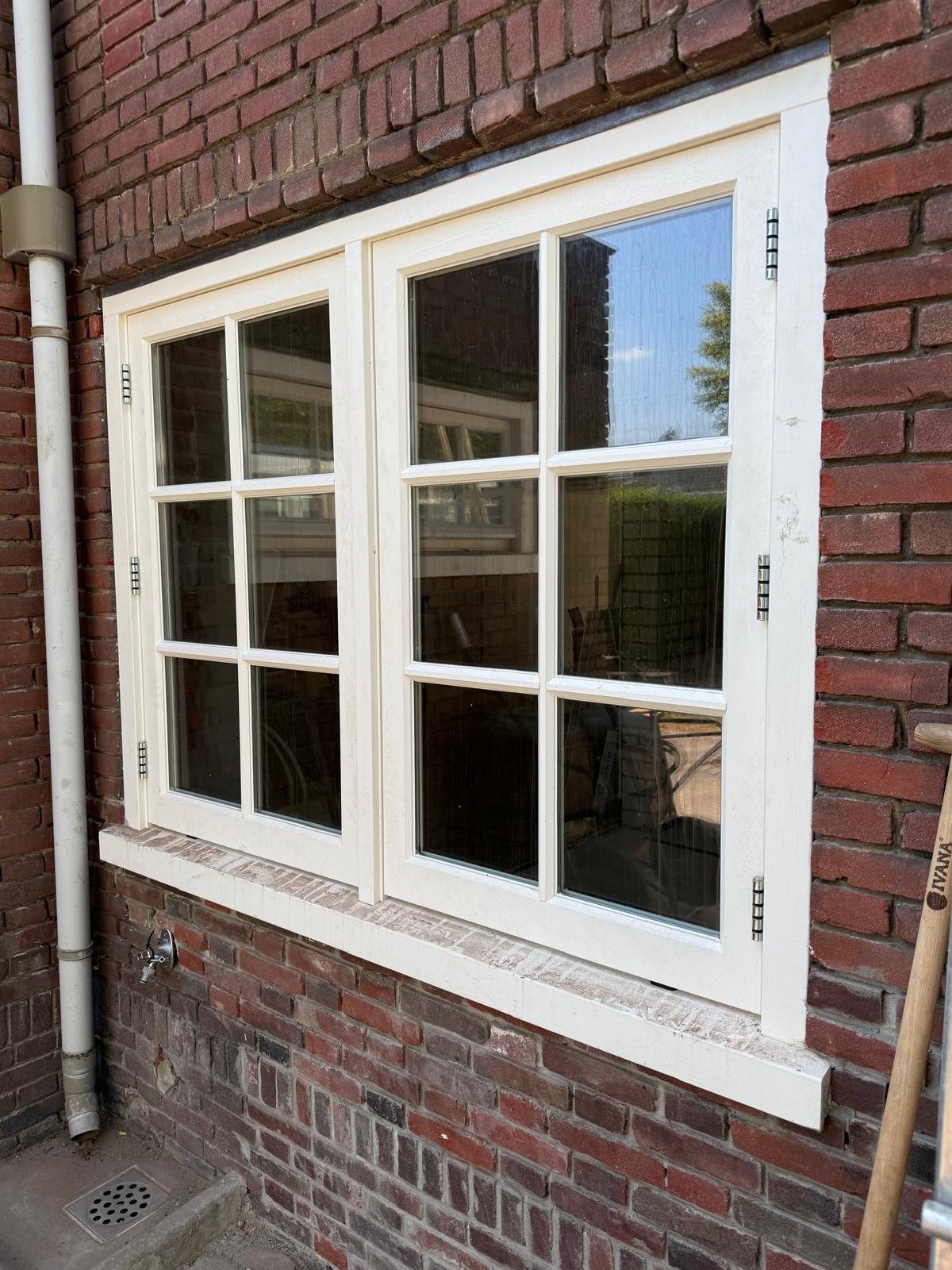 Afgewerkte houten kozijnen met roedeverdeling in een bakstenen gevel